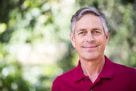 Smiling older man in red polo shirt with a blurred green background